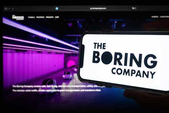 Silhouette of Hand Holding Phone with The Boring Company Logo in Front of Tunnel Construction Computer Screen