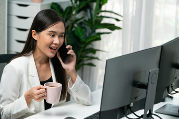 Working young Asian businesswoman calling to customer to present marketing online analysis service while drinking coffee, analyzing on social media website to plan channel sales target. Stratagem.