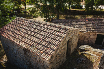 A traditional stone building with a rustic tiled roof, surrounded by greenery and casting natural shadows