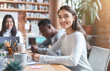 Fototapeta premium Close up of positive mixed race young woman attending business meeting in office, sitting with international colleagues around table