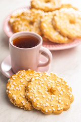 Sweet cookies in the shape of a flower. Tasty biscuits and cup of tea on white table.