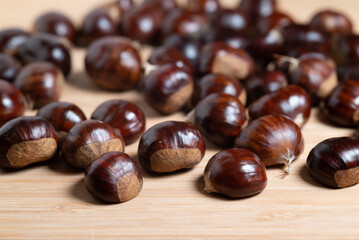 Pile of fresh raw chestnuts with shiny brown shells on a wooden table