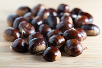 Fresh raw chestnuts with shiny brown shells on a wooden table
