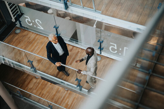High angle view of bald businessman discussing with senior male colleague while standing by glass railing