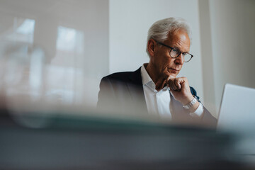 Businessman wearing eyeglasses with hand on chin working at office