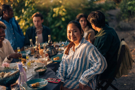 Portrait of smiling woman sitting with friends at dining table during party in back yard