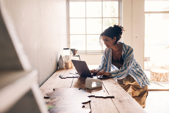Female designer working on laptop while leaning at table in workshop