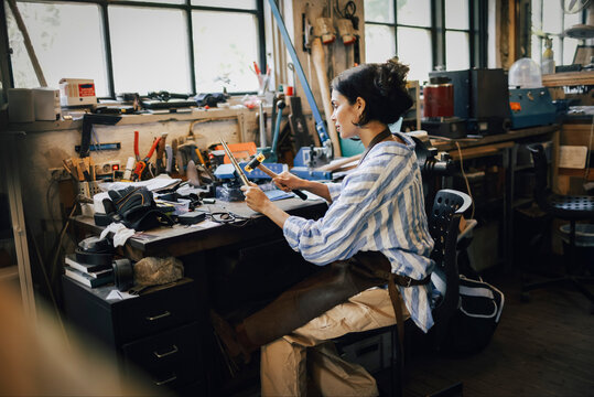 Side view of female craftsperson resizing jewelry while sitting on chair at workshop