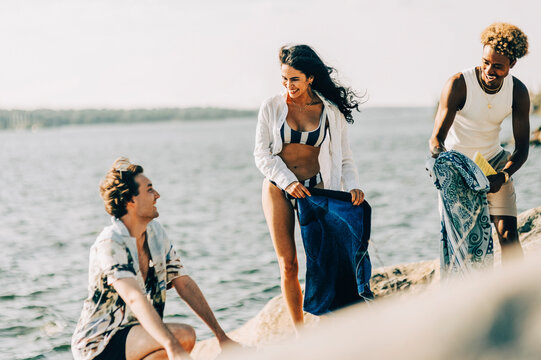 Happy male and female friends talking with each other while packing stuff after swimming at lake