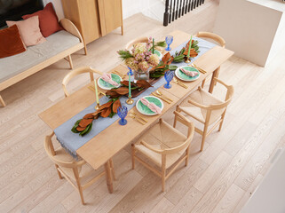 Elegant dining table setup with natural decor, including a greenery garland, pastel plates, blue glasses, and gold flatware, creating a cozy, modern ambiance for gatherings or celebrations.