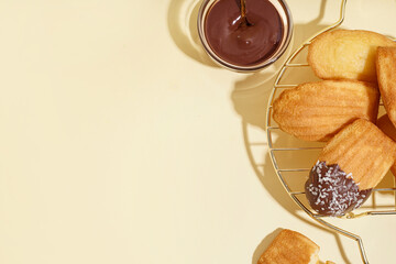Grid with delicious madeleines and bowl of chocolate paste on beige background