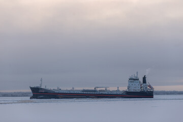 A large ship is peacefully floating on the water on a cloudy day, making for an interesting sight against the overcast sky