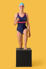 Happy young female swimmer on springboard against yellow background