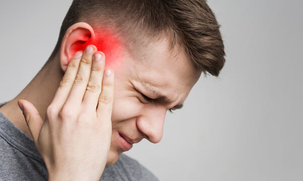 Young man has sore ear, suffering from otitis, touching his inflamed head, close up, empty space