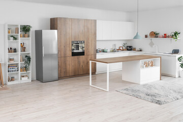 Interior of light kitchen with silver fridge, white counters and shelf unit