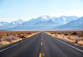Stretching highway through arid landscape leading towards snow-capped mountains in the distance under clear skies