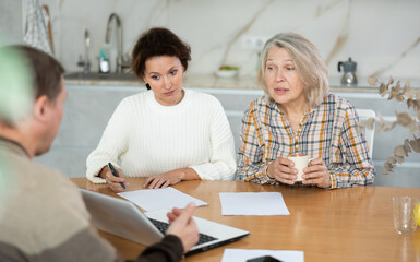 Obraz premium Two female family members trying to reach agreement with man agent sitting opposite to them in the kitchen