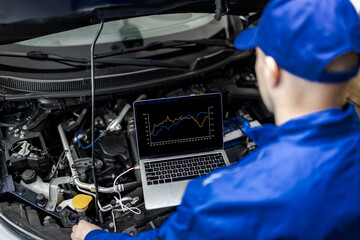 A mechanic analyzes engine data on a laptop during a vehicle inspection under the hood in a garage setting