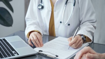 Doctor completing paperwork with patient. Close-up of a doctor's hands with forms, imparting information to a laptop. Medicine and health care concept