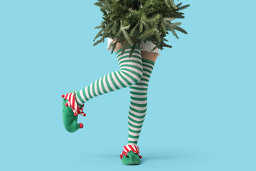 Legs of young woman in elf shoes with fir tree on blue background