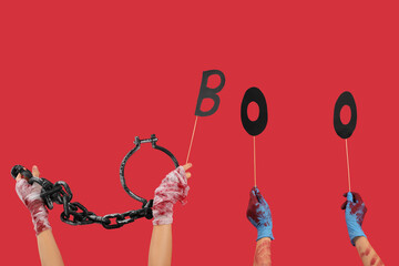 Hands of zombies with shackles and word BOO on red background. Halloween celebration