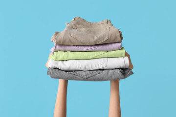 Female hands with stack of jeans on blue background