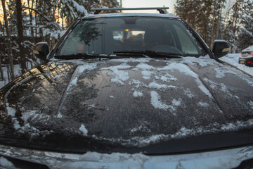 The hood of a car parked outside is completely coated in a thick layer of pristine snow, reflecting the beautiful winter scenery