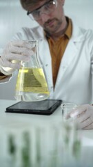 Man scientist wearing white protective gloves, and glasses is holding a yellow chemical solution...