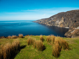 Obraz premium Stunning picturesque view on Slieve league cliffs, county Donegal, Ireland. Warm sunny day. Irish landscape scene. Blue cloudy sky and ocean surface, rough and tall cliffs.