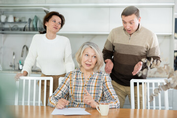 Competitive middle-aged man and woman conflicting and old woman writing inheritance sitting at...