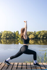 A woman is doing a yoga pose on a dock by a lake