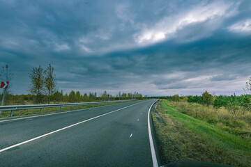 A road with a few trees in the background and a cloudy sky