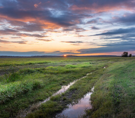 A field with a road running through it and a sunset in the background
