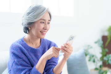 リビングでスマートフォンを使う中高年の女性 © taka