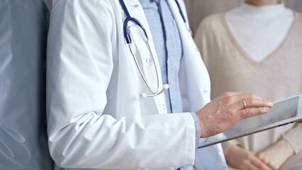 Doctor and patient. Close-up of a doctor's hand taking notes on a clipboard with a woman in the...