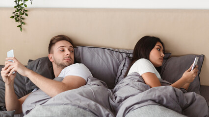 Infidelity. Jealous Husband Peeking At Wife's Phone Lying In Bed And Texting, Suspecting Affair At Home