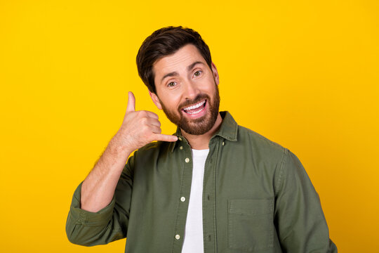 Portrait of nice young man show call me symbol wear khaki shirt isolated on yellow color background
