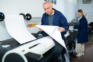 Caucasian man working in printing office, using large format printer.