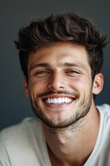 Obraz premium Young man with a beautiful smile on a grey background, ideal for dental ads.