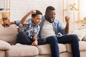 Obraz premium Family Cheering. Afro Dad And Son Emotionally Supporting Their Favorite Team, Watching Sports On Tv At Home Together, Free Space