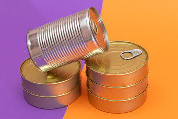 A Group of Stacked Tin Cans with Blank Edges on Split Orange and Violet Background. Canned Food. Different Aluminum Cans for Safe and Long Term Storage of Food. Steel Sealed Food Storage Containers