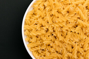 Uncooked Fusilli Pasta Lying on White Plate on Black Background. Raw and Dry Macaroni. Unhealthy and Fat Food - Top View