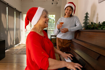 Christmas time, Senior female friends wearing Santa hats enjoying piano music and wine at home