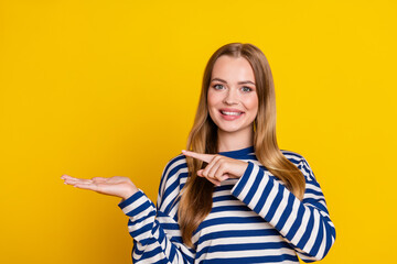 Photo of lovely cute woman wear striped stylish pullover arm hold empty space isolated on yellow color background