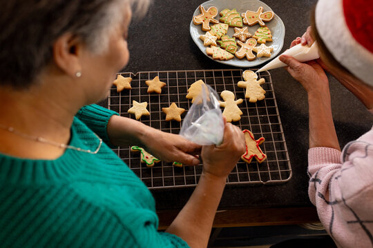Decorating Christmas cookies, senior female friends in cozy kitchen sharing holiday spirit, at home
