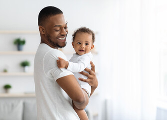 Happiness Of Fatherhood. Portrait of young black dad with cute little baby on his hands standing...