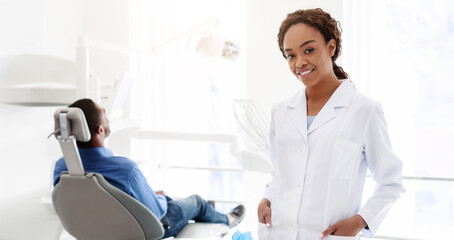 Obraz premium Pretty african american woman dentist smiling over stomatological cabinet, copy space
