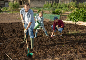 Farmer with a shovel drips a garden to plant seeds. Man with his family works on a farm and...