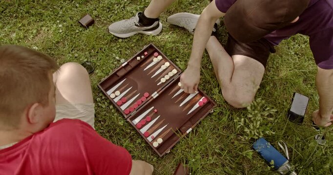 Two friends enjoy a leisurely game of backgammon in the park, showcasing camaraderie and outdoor fun.