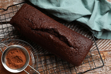 Tasty chocolate sponge cake and cocoa powder on wooden table, flat lay